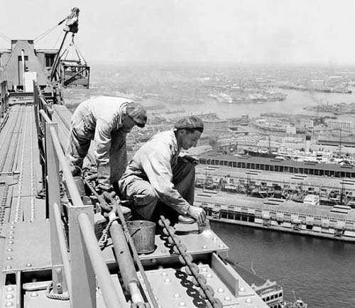 Two painters wearing overalls but no harness or safety equiment are painting the bridge in 1949