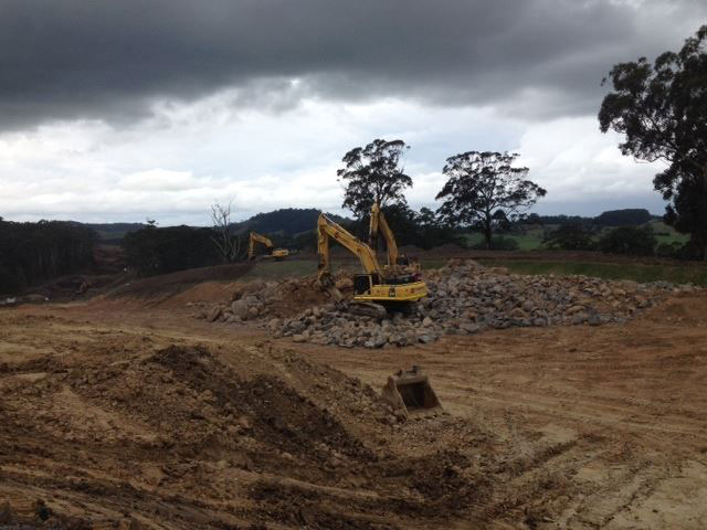 Two excavators breaking down large rocks in preparation for processing and use as construction mater