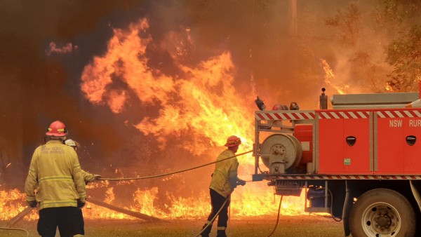 Two men and a firetruck get ready to fight a huge bushfire beyond them. 