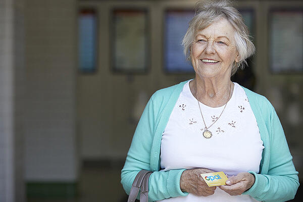 An elderly lady poses smiling with her yellow senior opal card
