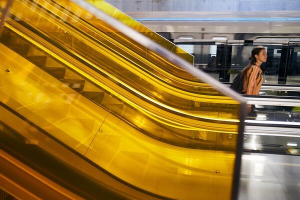 A commuter exits the escalator on Bella Vista platform. They are framed by sunflower yellow glass which runs alongside the escalator.