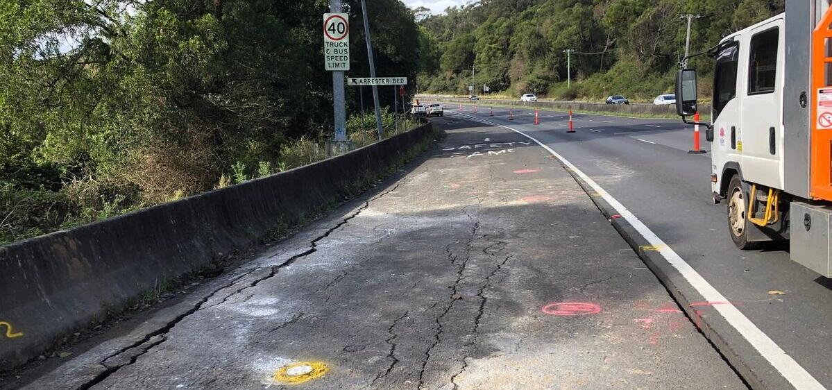 A photo of a work truck parked beside a road that has extensive crack damage visible in the pavement.