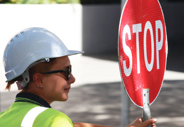 Woman in hard hat and hi-vis holds stop sign