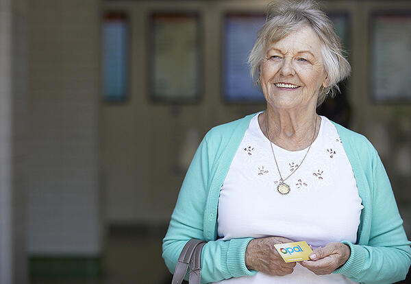 An elderly lady poses smiling with her yellow senior opal card