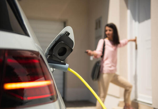 Electric vehicles - woman enters home after charging EV